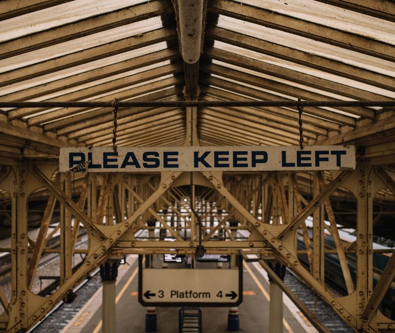The image depicts an exterior view of Crystal Palace train station with a partially covered platform area featuring a metal and glass roof structure. The platform surface is made of concrete with tact