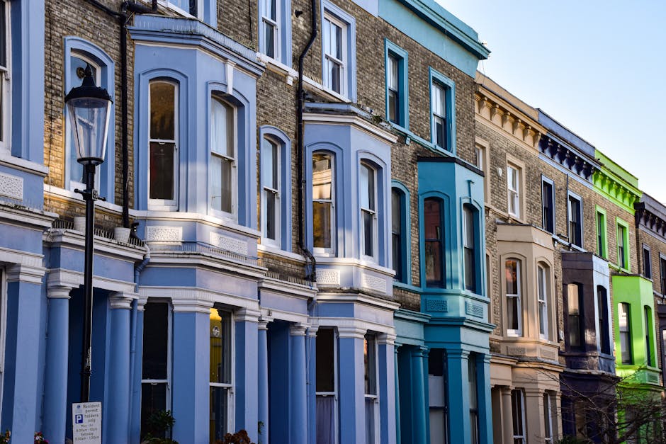Photograph of a row of Victorian terraced houses on Westow Hill in Crystal Palace, showcasing colorful facades with three-story bays, large sash windows, and decorative architectural details. The hous